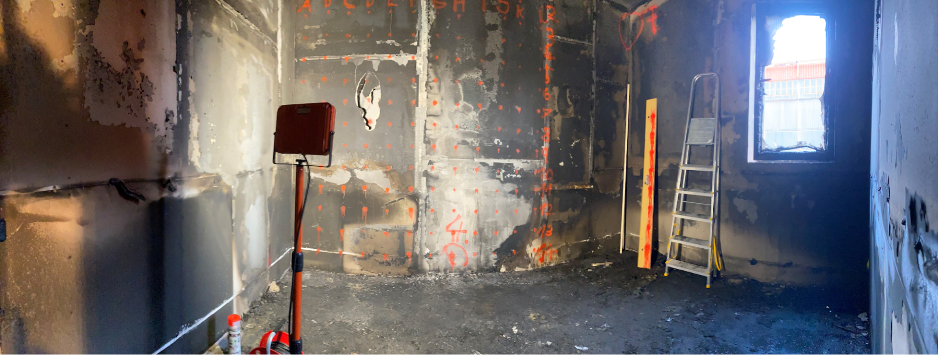 Fire-damaged gypsum board walls with marked measurement positions inside an experimental office.